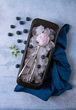 Yaban mersinli dondurma, kaşıklı kap gri bir masada, taze yaban mersinli.,