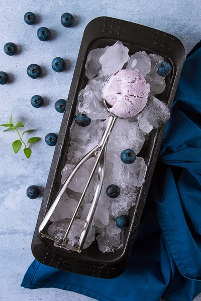 Blueberry ice cream, container with a spoon, on a gray table, fresh blueberries,