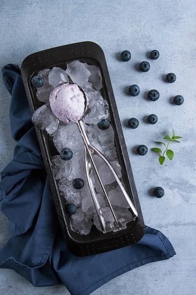 Blueberry ice cream, container with a spoon, on a gray table, fresh blueberries,