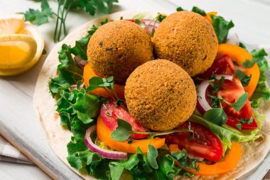 Tortillas, wrapped falafel balls, with fresh vegetables, vegetarian healthy food, on a wooden white background, no people, selective focus.