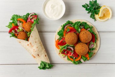 Tortillas, wrapped falafel balls, with fresh vegetables, vegetarian healthy food, on a wooden white background, no people, selective focus.