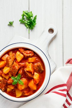 Etli, domates soslu, baharatlı ve otsuz patatesler beyaz bir masada.,