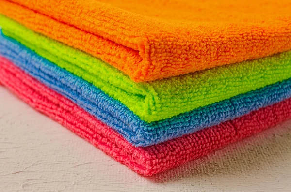 A stack of colored cloth , microfiber, for cleaning the house, on a white table, horizontal, no people,