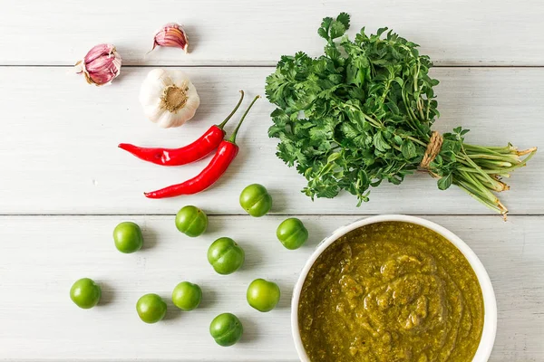 Tkemali sauce, traditional Georgian cuisine, green cherry plum, with ingredients for sauce, cilantro, mint, hot pepper, garlic, on a white wooden table, close-up, rustic, food background, no people, selective focus, sauce, green sauce, tkemali, georg