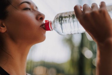 Siyah spor giysili genç bir kadın parkta esniyor ve spor yapıyor. Molada su içen çekici fit bir kız. Sağlıklı yaşam tarzı kavramı.