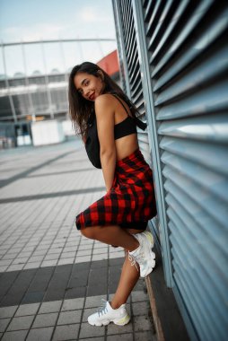 Paten kayan bir gencin yanında durmak limonata ve bel çantasıyla duvarı kör eder. Yaz şehrinde kırmızı kare gömlekli bir kız.