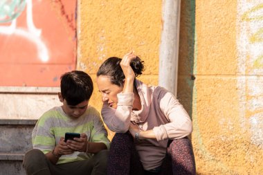 Anne ve oğul cep telefonlarına bakın. Sokakta oturuyorlar..