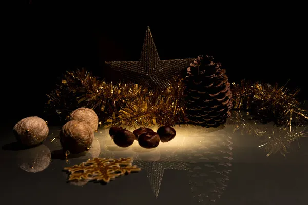 Kerstmis ornamenten en kastanjes op een glazen tafel met een gouden ananas slinger en ster op een zwarte achtergrond — Stockfoto