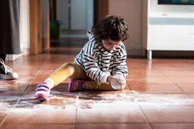 Küçük kız hamurla oynuyor. Mutfakta yerde oturuyor.