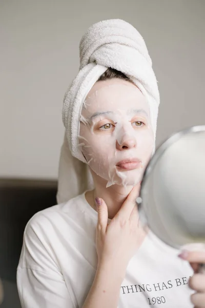 頭にタオルをつけた若い女性顔に化粧品のマスクシート — ストック写真