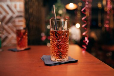 A glass of a refreshing red drink with ice, lit by a lamp on the background.