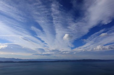 Mavi gökyüzü, denizin üstünde beyaz bulutlar