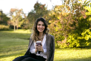 Parkta hazır kahve içen güzel genç bir kadın. Açık havada kahve fincanıyla güzel bir kızın ön portresi..