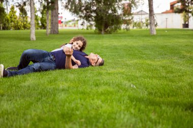 Full length image of a niece hugs her grandfather in the park on a sunny day, they lie on the green grass. clipart