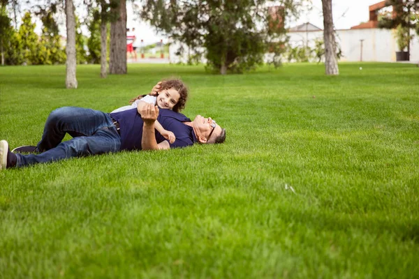 Full length image of a niece hugs her grandfather in the park on a sunny day, they lie on the green grass. — Stock Photo, Image