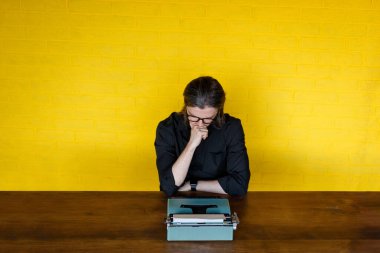 Masada oturan, daktiloya bakan, sarı duvarın üzerinde ilham almayan düşünceli bir adamın üst görüntüsü..