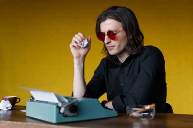 Masada oturan bir yazarın profili daktilo üzerinde çalışıyor, buruşmuş kağıtlar, sarı arka plan üzerinde..