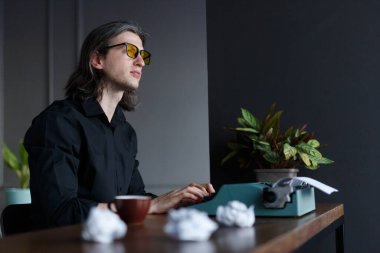 Yeni kitabı düşünen, eski bir daktilo üzerinde çalışan, ofisteki bir masada oturan zeki genç bir yazar..