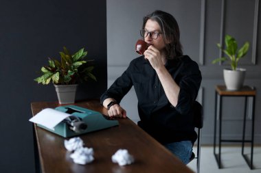 Siyah gömlekli ve gözlüklü genç adam, çalışma masasında kahve içiyor iş fikri için, gri iç mekanlarda..