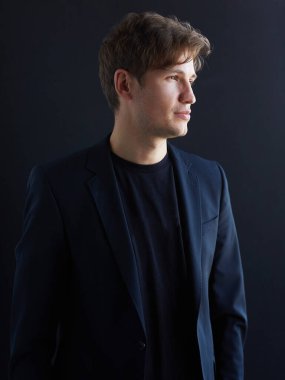 Siyah arka planda ceketli çekici genç bir işadamının profil portresi..