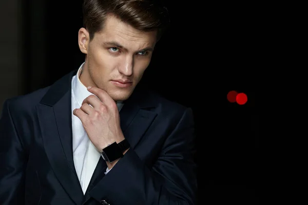 Retrato frontal de um belo empresário posando em terno preto, usar relógio na mão, fundo preto isolado. — Fotografia de Stock