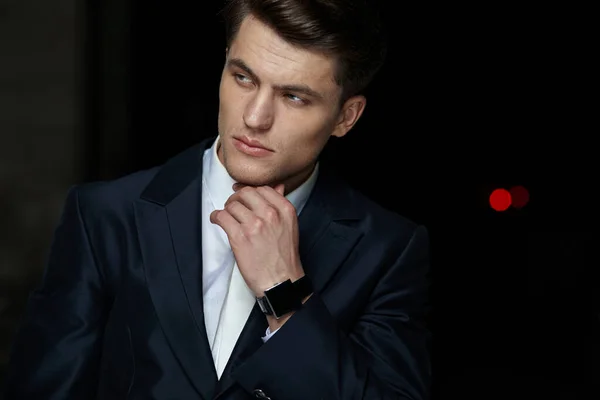 Perfil retrato de um empresário bonito posando em terno preto, usar relógio em sua mão, fundo preto isolado. — Fotografia de Stock