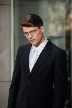 Gözlüklü, siyah takım elbiseli, beyaz kravatlı ve gömlekli esmer bir işadamının profil portresi..