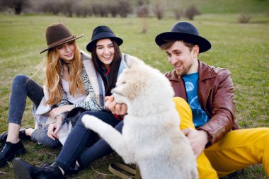 Üç güzel, genç ve şık arkadaş birlikte dışarıda vakit geçiriyorlar. İri köpekleri yeşil çimlerin üzerinde oturuyor..