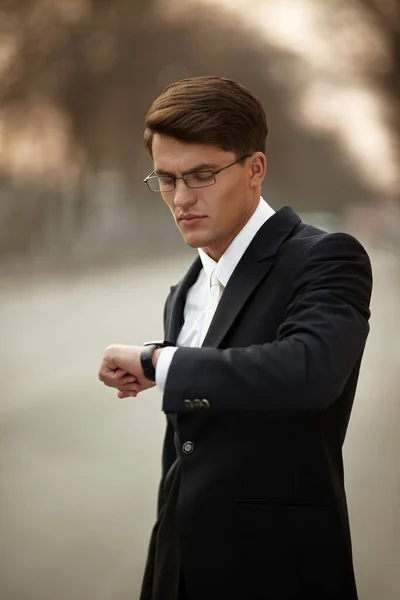 Portret dorosłego modela w okularach. Biznesmen w czarnym garniturze i białym krawacie, patrzący na zegarek. — Zdjęcie stockowe