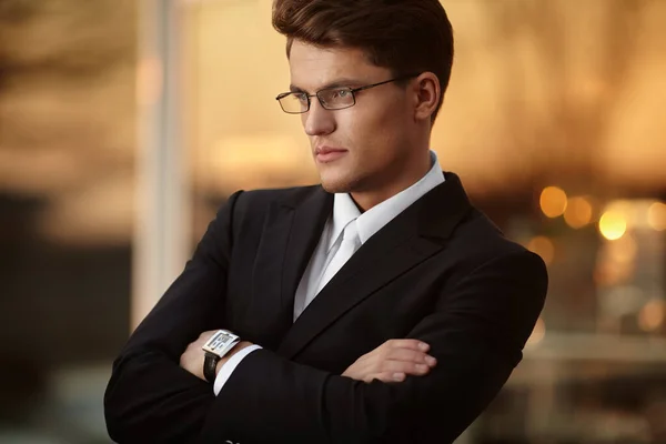 Closeup profile of a handsome businessman with crossed arms in eyeglasses and black suit, wear watch on his hand. — Stock Photo, Image