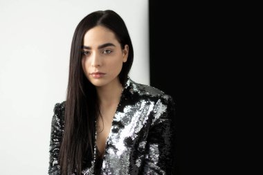 Gümüş ceketli esmer bir kızın portresi. Makyajlı, kaşlı, beyaz ve siyah arkaplanlı..