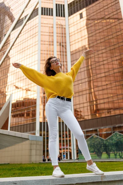 Нижний вид молодой женщины носить в желтом свитере и белых джинсах, сидящих с поднятой рукой в дневное время. — стоковое фото