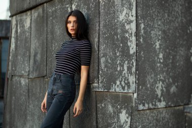 Siyah modaya uygun, zayıf vücutlu seksi esmer kadın, eski duvarın yanında durup kameraya bakıyor..