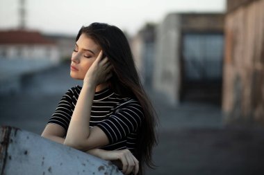 Kendine güvenen genç bir kızın profil portresi, düz saçlı, çatıda, gün batımında.