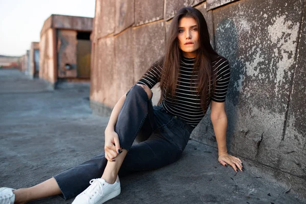 Chica joven con mirada confiada, cabello liso, mirando a la cámara, sentada en el techo, en la luz del atardecer. —  Fotos de Stock