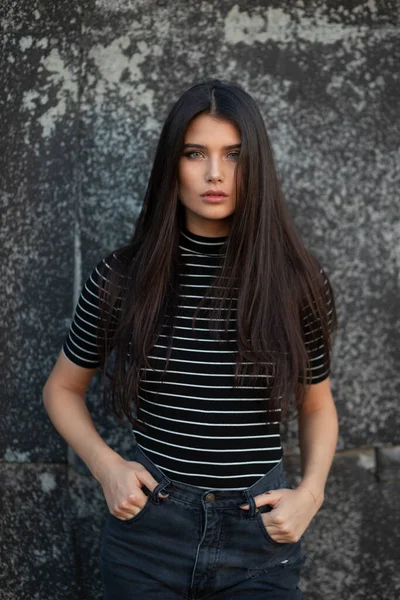 Szépség frontális portré egy vidám lány egyenes haj, öltözött modern ruhák, smink, támogatja a fal. — Stock Fotó