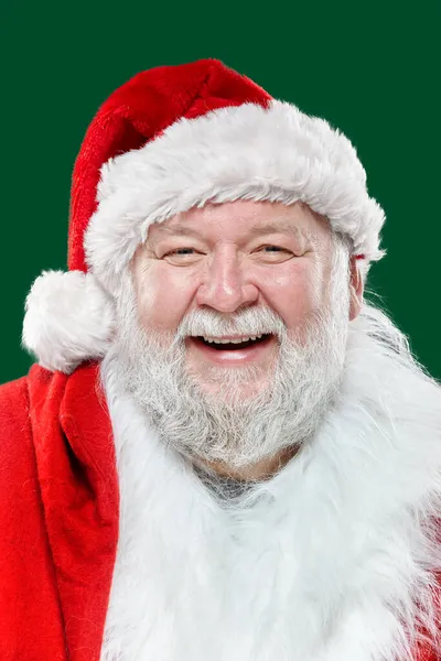 Closeup portrait of a happy laughing Santa Claus in a red coat and a hat, isolated green background. — Stock Photo, Image