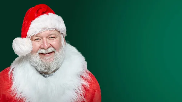 Imagem de perto de um Papai Noel feliz vestido com um casaco vermelho e um chapéu, fundo verde isolado. Espaço para texto. — Fotografia de Stock