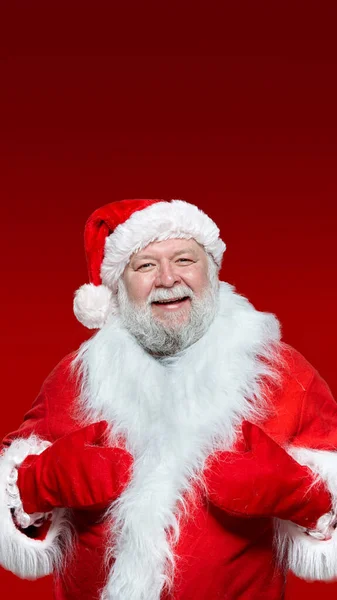 Primer plano de un feliz Papá Noel con un abrigo rojo, guantes y un sombrero, con las manos en alto, fondo rojo aislado. —  Fotos de Stock