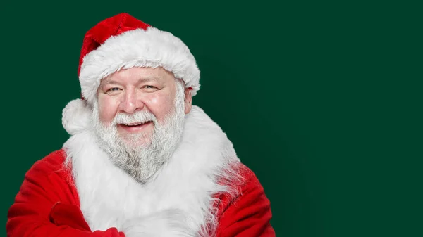 Imagen de primer plano de un feliz Santa Claus riendo vestido con un abrigo rojo y un sombrero, fondo verde. Espacio para texto. —  Fotos de Stock