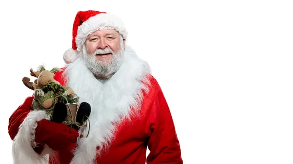 Happy Santa Claus in a red coat, gloves and a hat, holding a toy in hands, pointing his finger, white background. — Stock Photo, Image