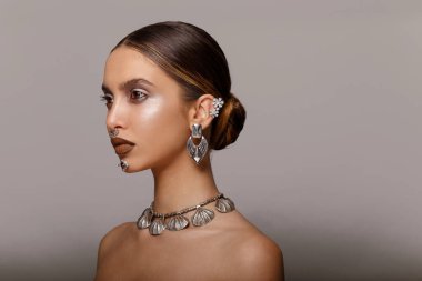Yatay görüş. Moda güzellik modeli, profesyonel makyaj ve güzel mücevherler, çıplak omuzlar, profil pozu, stüdyo, gri arka plan.