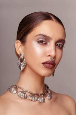 Şehvetli kadın modeli, bronz tenli, makyajlı, gümüş antika bijouterie 'li gri arka planda kameraya bakan..