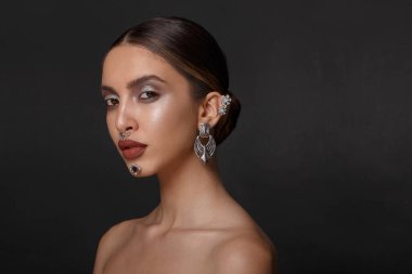 Makyajlı bir kızın portresi, profilde çıplak omuzlar, mücevherler, siyah arka plan, kopyalama alanı.