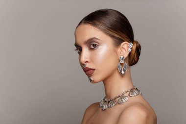 Gri arka planda, bordo dudaklı, kirpikli ve mücevherli bir model. Güzel kadın yüzü, güzel makyaj..