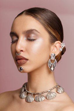 Gözleri kapalı, saç stili, makyajı, büyük dudakları, takıları, stüdyo görüntüleri, koyu pembe arka planı olan bir manken..