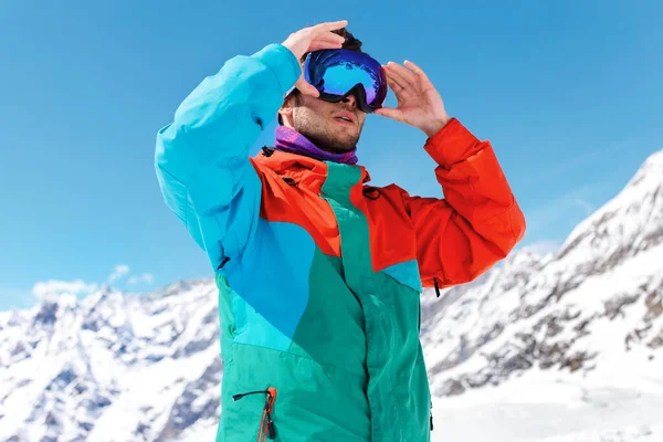 若いスキーヤーの水平方向の肖像画は 山やカラフルな服にスキーグラスを着て 澄んだ空と晴れた日の背景に座っている 観光コンセプト — ストック写真