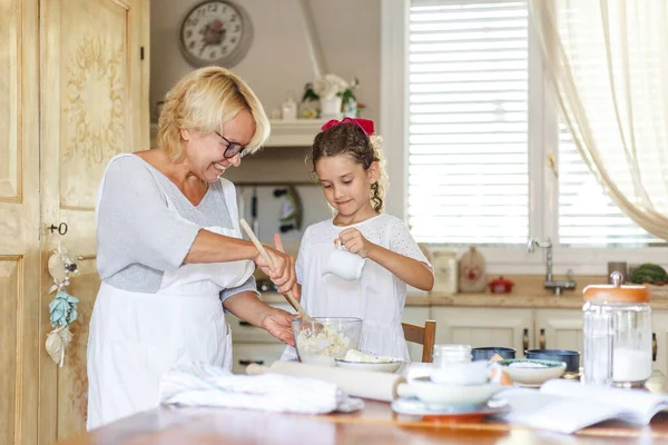 Šťastná babička a roztomilá malá kudrnatá vnučka v kuchyni, připravují se spolu. — Stock fotografie
