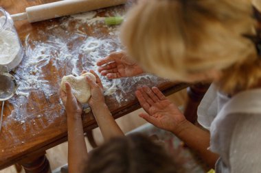 Kalp şeklinde mangır tutan bir kadın ve çocuk elinin üst görüntüsü. Koyu masada malzemeler pişiriyorum.