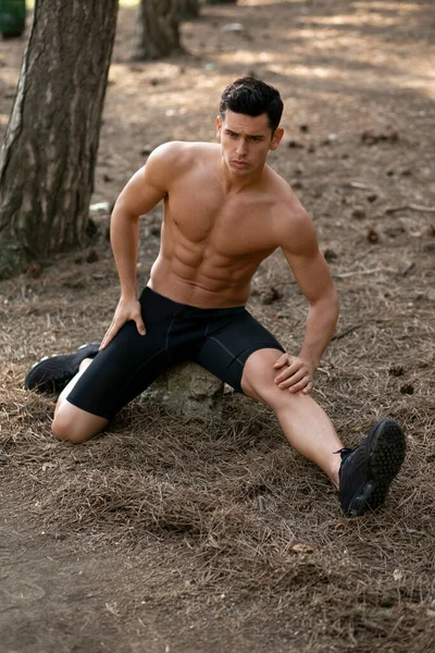 Full length image of a athletic sportsman doing stretching exercises in the park. — Stockfoto